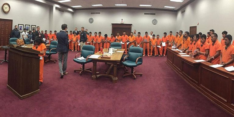 A photo from inside a court room for a mass trial of immigrants, dressed in bright orange jumpsuits in a long line, at the Lucius D. Bunton Federal Courthouse in Pecos, Texas in 2018.
