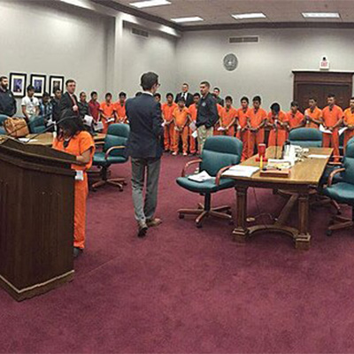 A photo from inside a court room for a mass trial of immigrants, dressed in bright orange jumpsuits in a long line, at the Lucius D. Bunton Federal Courthouse in Pecos, Texas in 2018.